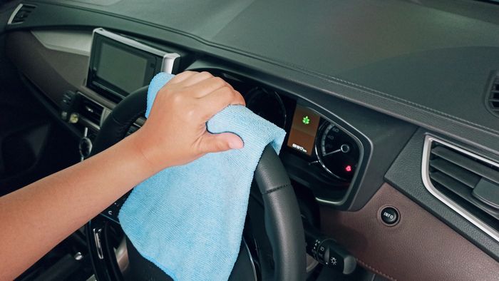 A person detailing a car interior dashboard with a microfibre cloth