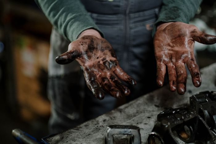 A mechanic's grease-stained hands in a workshop setting, illustrating the need for heavy-duty hand cleaning